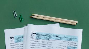 IRS tax forms on green background with two pencils and paperclips