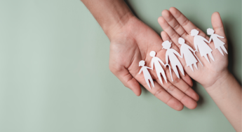 open hands holding paper cutout of family