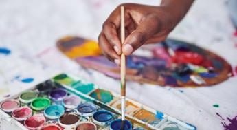 hand dipping paint brush into paint on white canvas