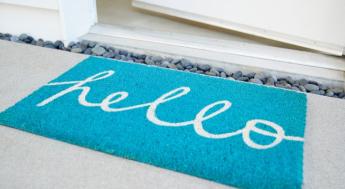 teal welcome matt that says hello on ground next to open door