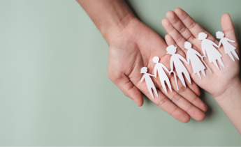 open hands holding paper cutout of family