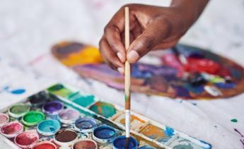 hand dipping paint brush into paint on white canvas