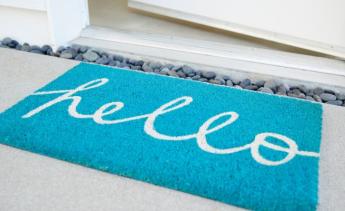 teal welcome matt that says hello on ground next to open door