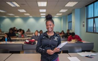 Student Standing in Classroom with Books Smiling