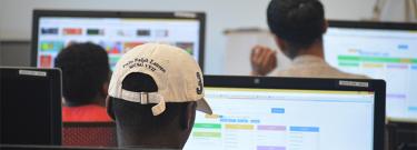 three male students look at computer screens with their backs to the camera.