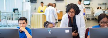 nursing students work in classroom and on computer while instructor assits