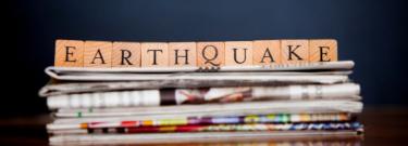 blocks spelling out earthquake on top of a stack of newspapers